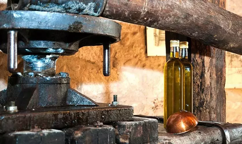 antico frantoio in primo paino e due bottiglie di olio sulla destra
